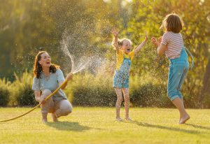 Children cool off on a hot summer day as their mom sprays a hose.
