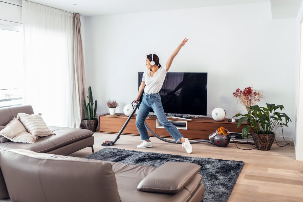 A woman dancing and listening to music through headphones while she cleaning her living room.