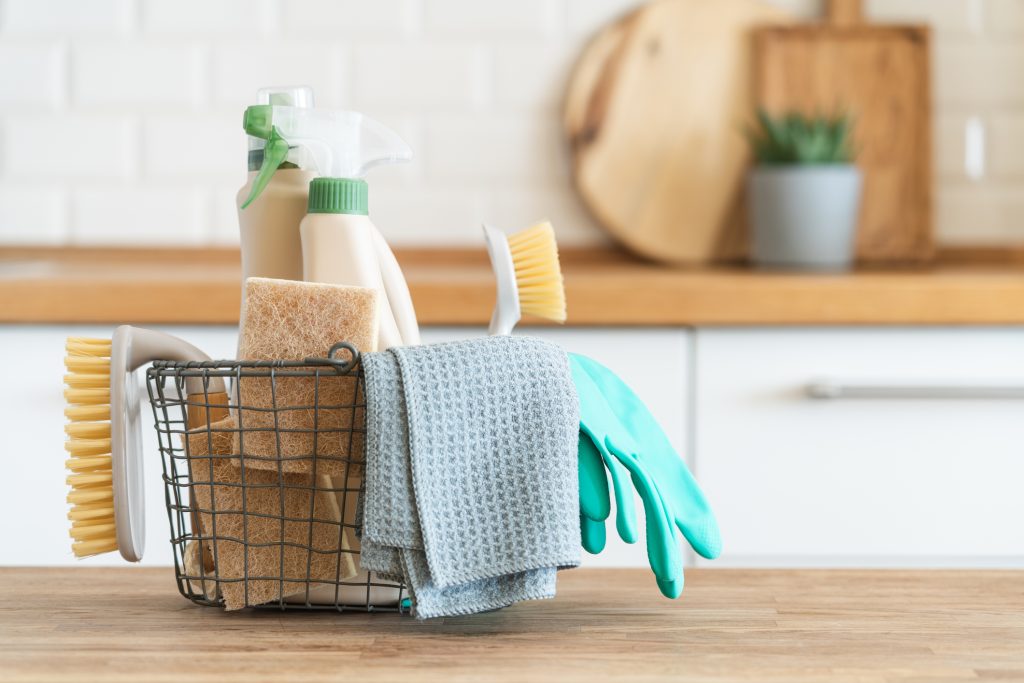 A bucket of various sprays and brushes on a countertop in an apartment representing spring cleaning.